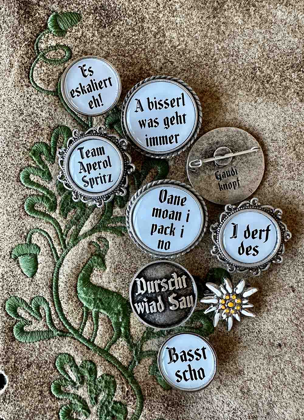 Verschiedene Anstecker mit bayerischen Sprüchen auf einer Lederhose.